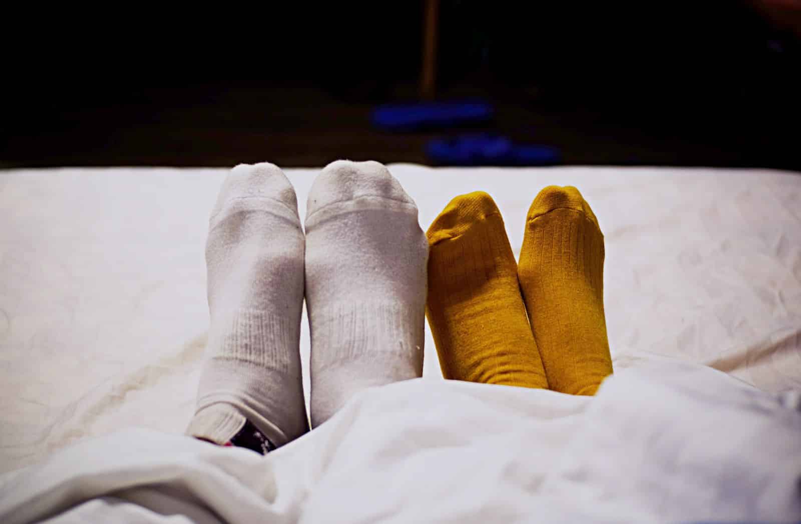 Deux paires de pieds en chaussettes dépareillées au lit, illustrant le froid aux pieds la nuit après 55 ans
