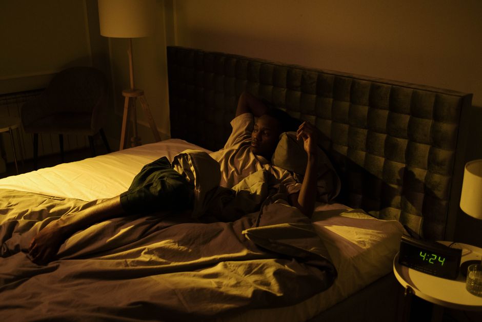 Homme réveillé la nuit dans un lit défait, couette rejetée, réveil affichant 4h24 — illustration des sueurs nocturnes après 55 ans